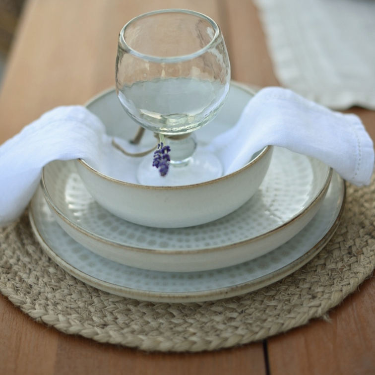 Set di stoviglie in ceramica bianca con piatti e ciotola su sottopiatto intrecciato con tovagliolo bianco