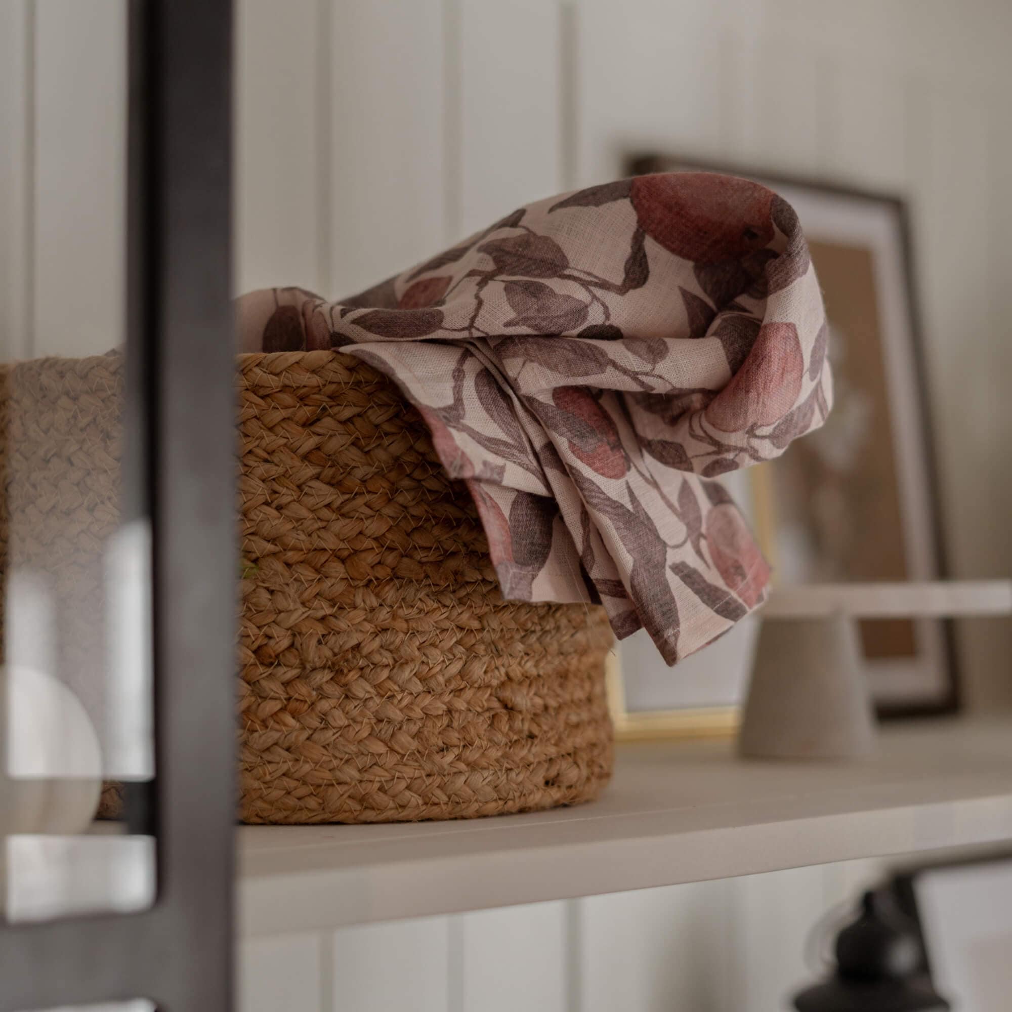 Cesto in materiale intrecciato naturale con tessuto di lino a motivo floreale rosa e marrone su mensola bianca