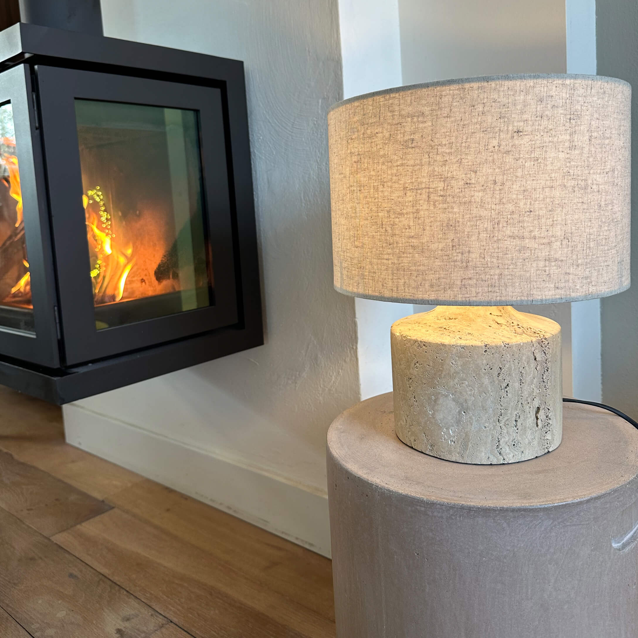 Lampada da tavolo con paralume beige e base in pietra chiara accanto a camino acceso