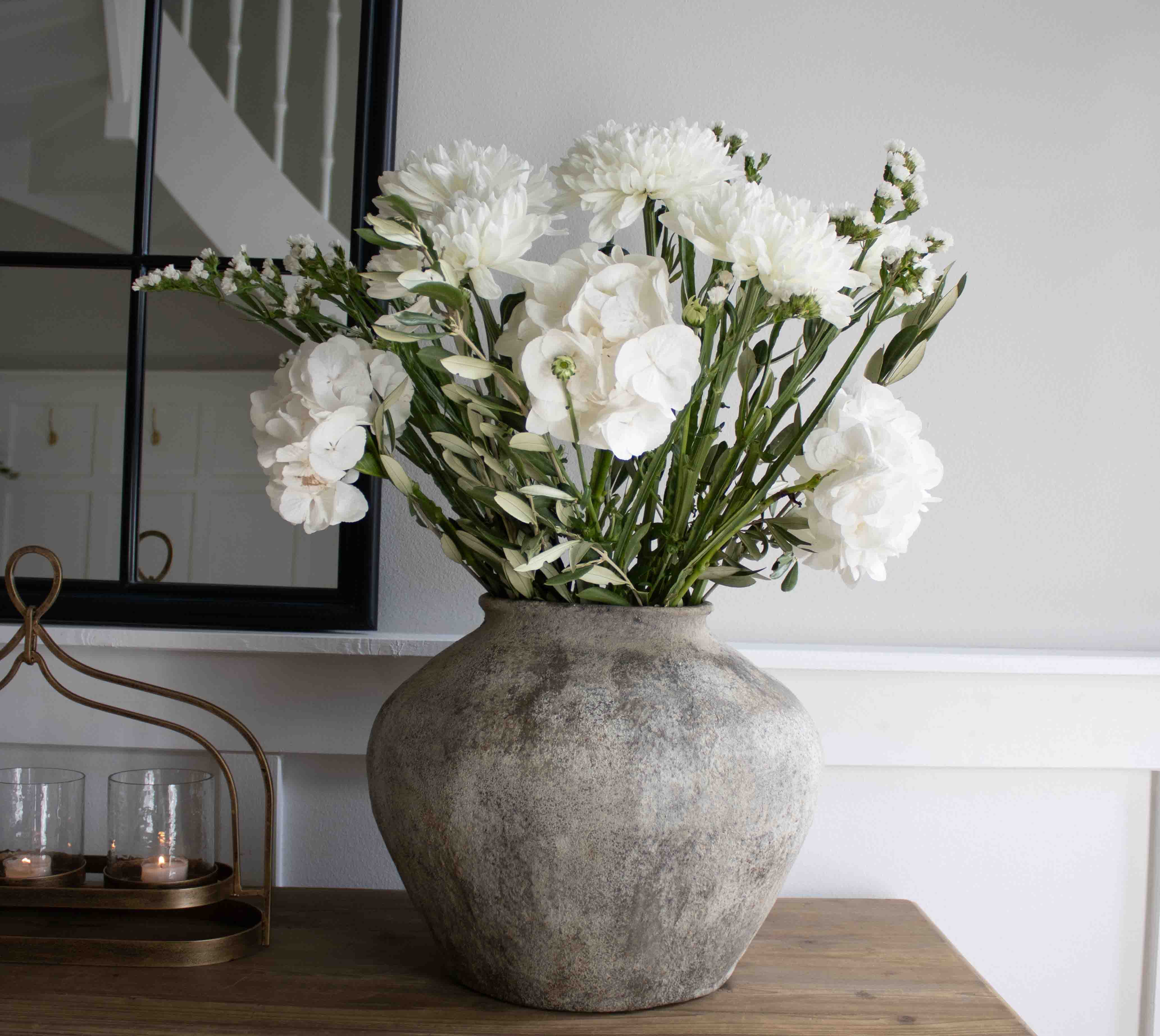 Grande vaso in pietra grigia con fiori bianchi decorativi su tavolo in legno in soggiorno