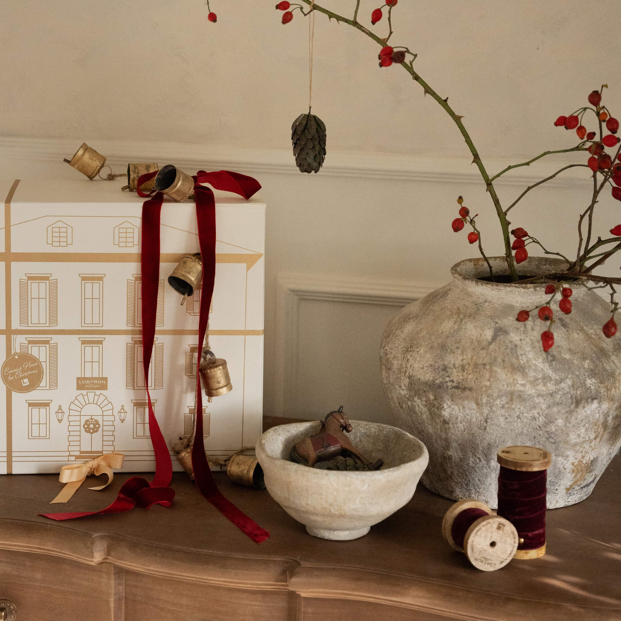 Composizione decorativa natalizia con nastri rossi, campanelli e ciotola in ceramica su tavolo in legno