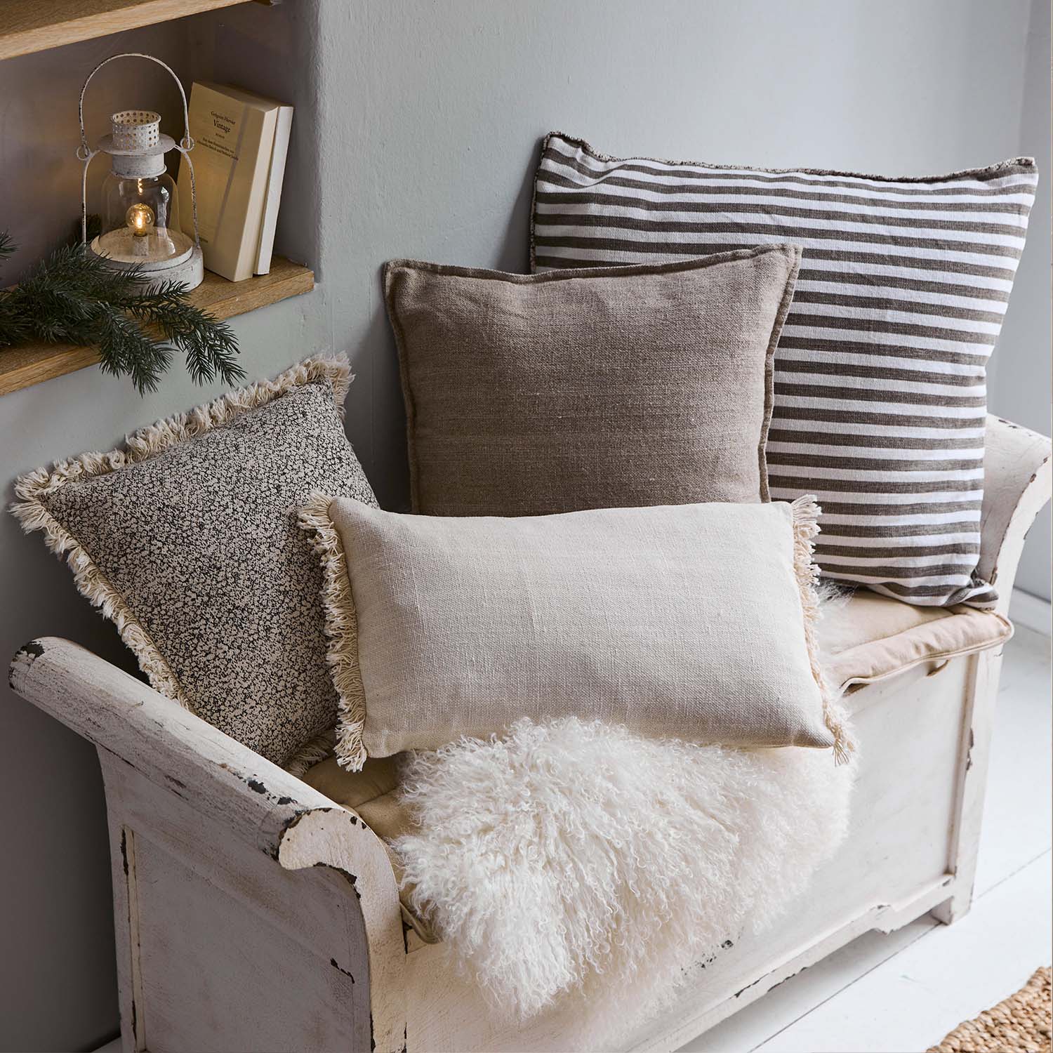 Set di cuscini decorativi beige e marroni su panca in legno bianco con coperta pelosa