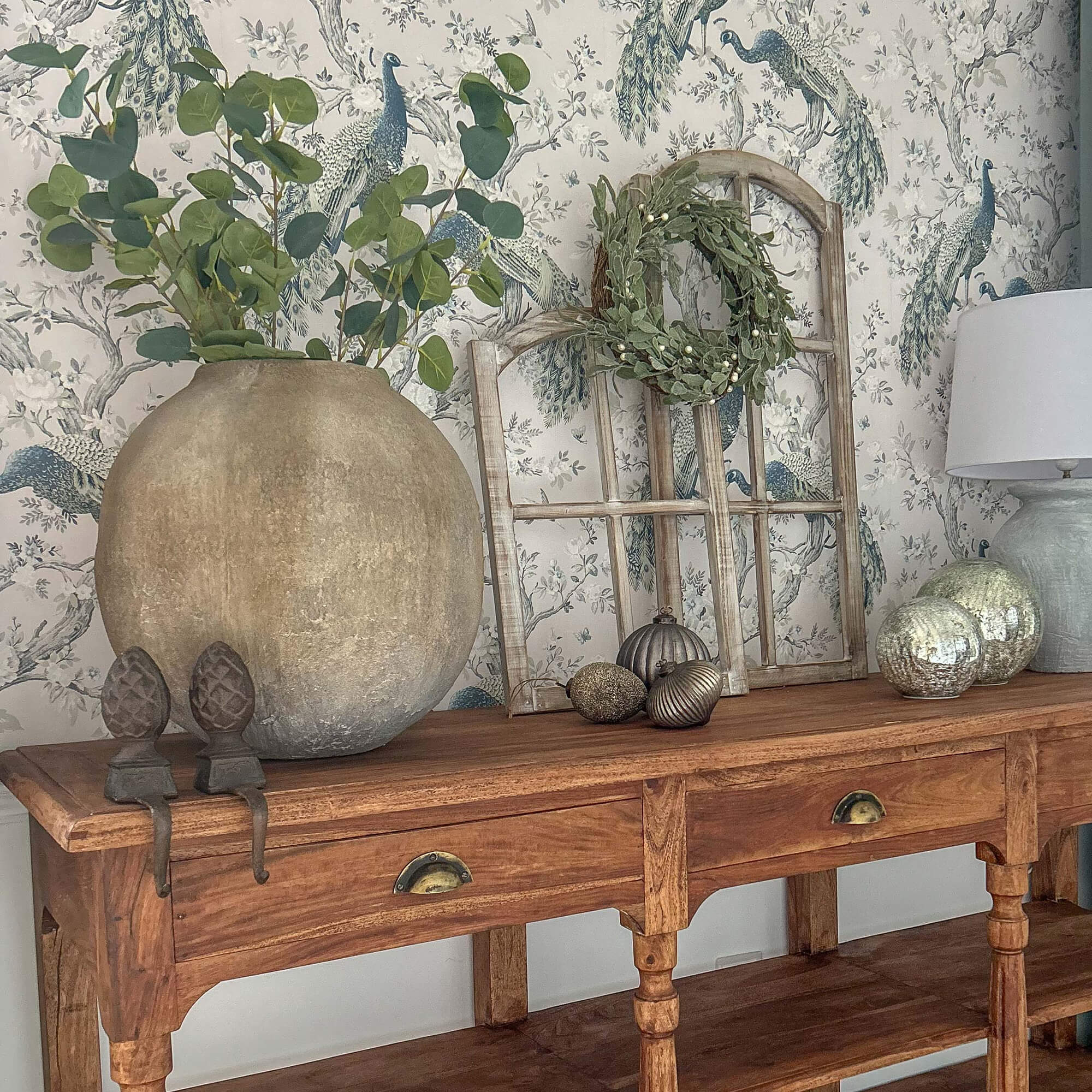 Tavolo in legno con grande vaso in terracotta, foglie verdi, lampada e decorazioni sopra
