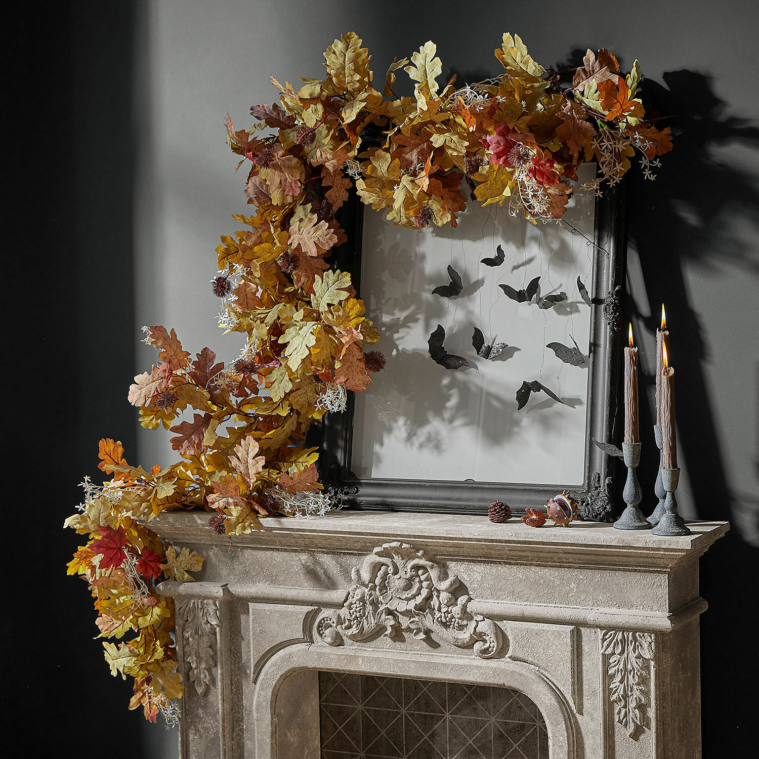 Festone Fleurimont Corona decorativa autunnale di foglie di quercia in tonalità calde su camino in pietra con cornice nera e candele