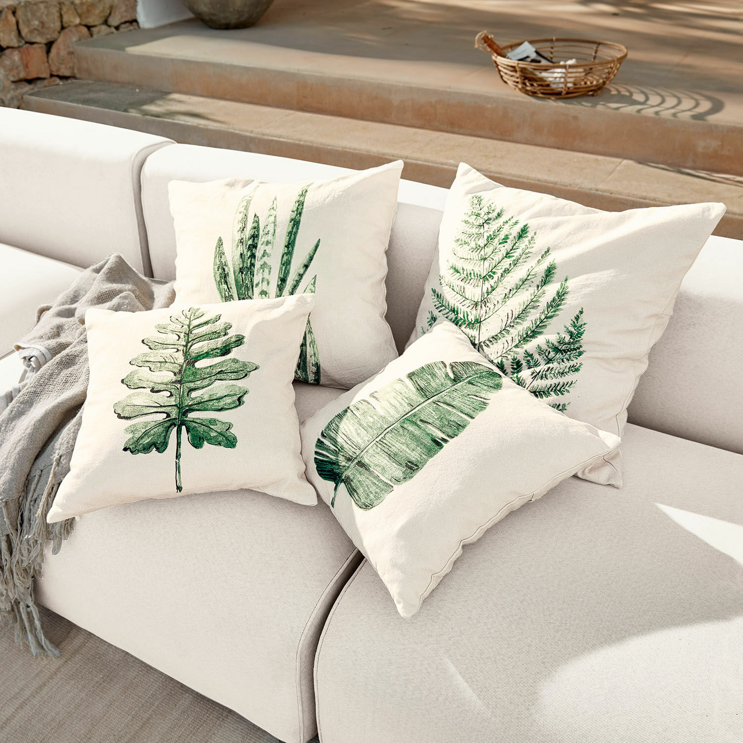 Set di 4 copricuscini Marly Set di quattro cuscini crema con stampe di foglie verdi su divano chiaro, decorazione casa