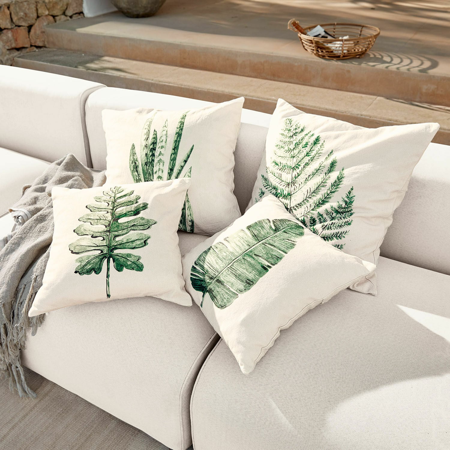 Set di 4 copricuscini Marly Set di quattro cuscini crema con stampe di foglie verdi su divano chiaro, decorazione casa