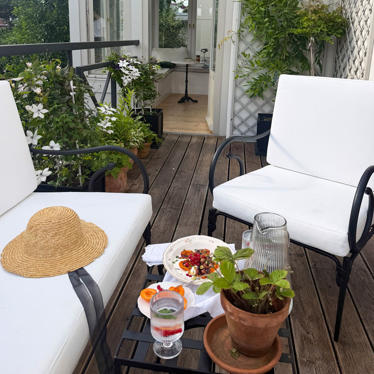 Terrazza con sedie in metallo bianche, pavimento in legno e piante in vaso per area relax