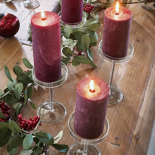 Candele rosse su portacandele in vetro trasparente su tavolo di legno con foglie verdi e bacche rosse
