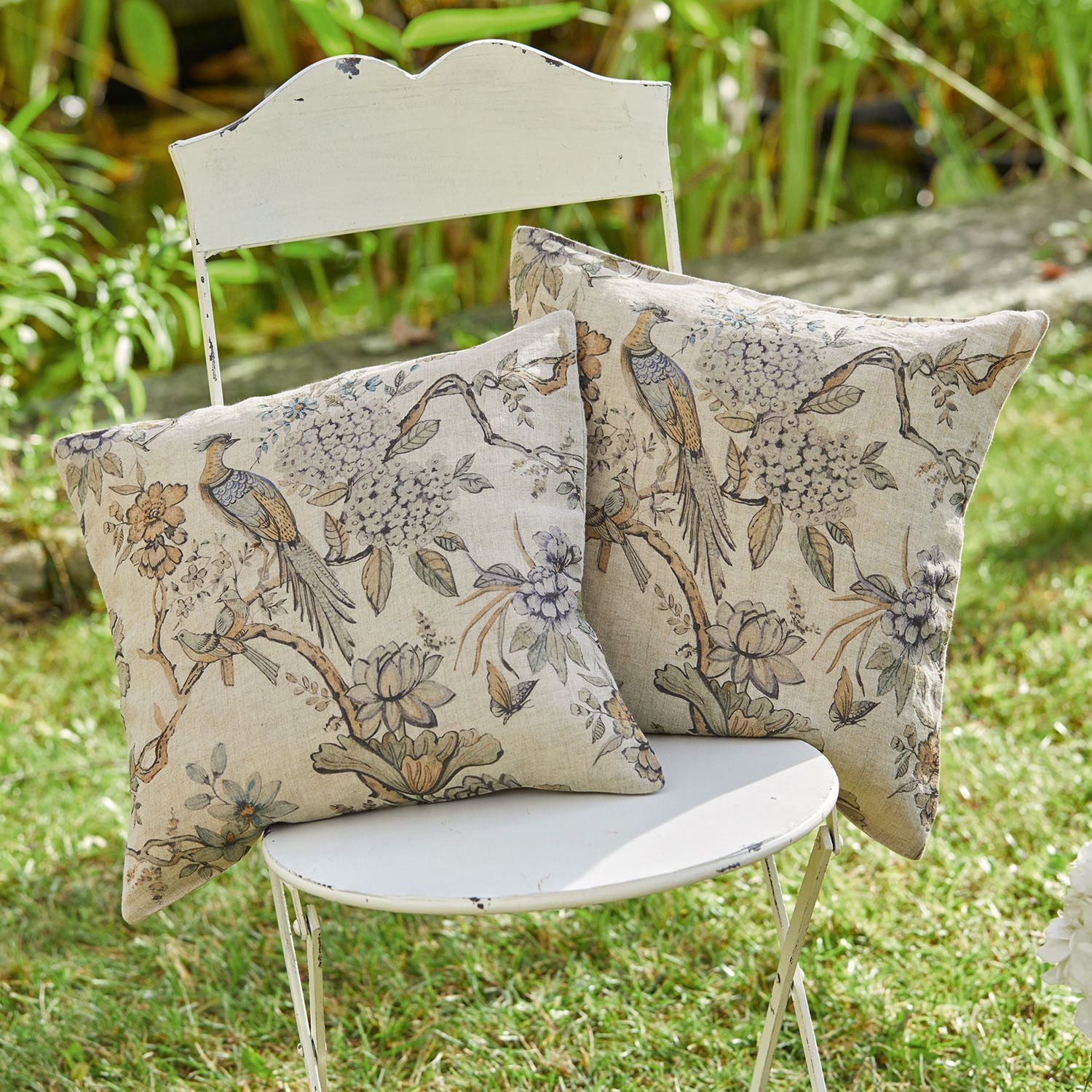 Coppia di copricuscini Lorry Due cuscini decorativi in cotone beige con stampa di uccelli e fiori su sedia bianca in giardino