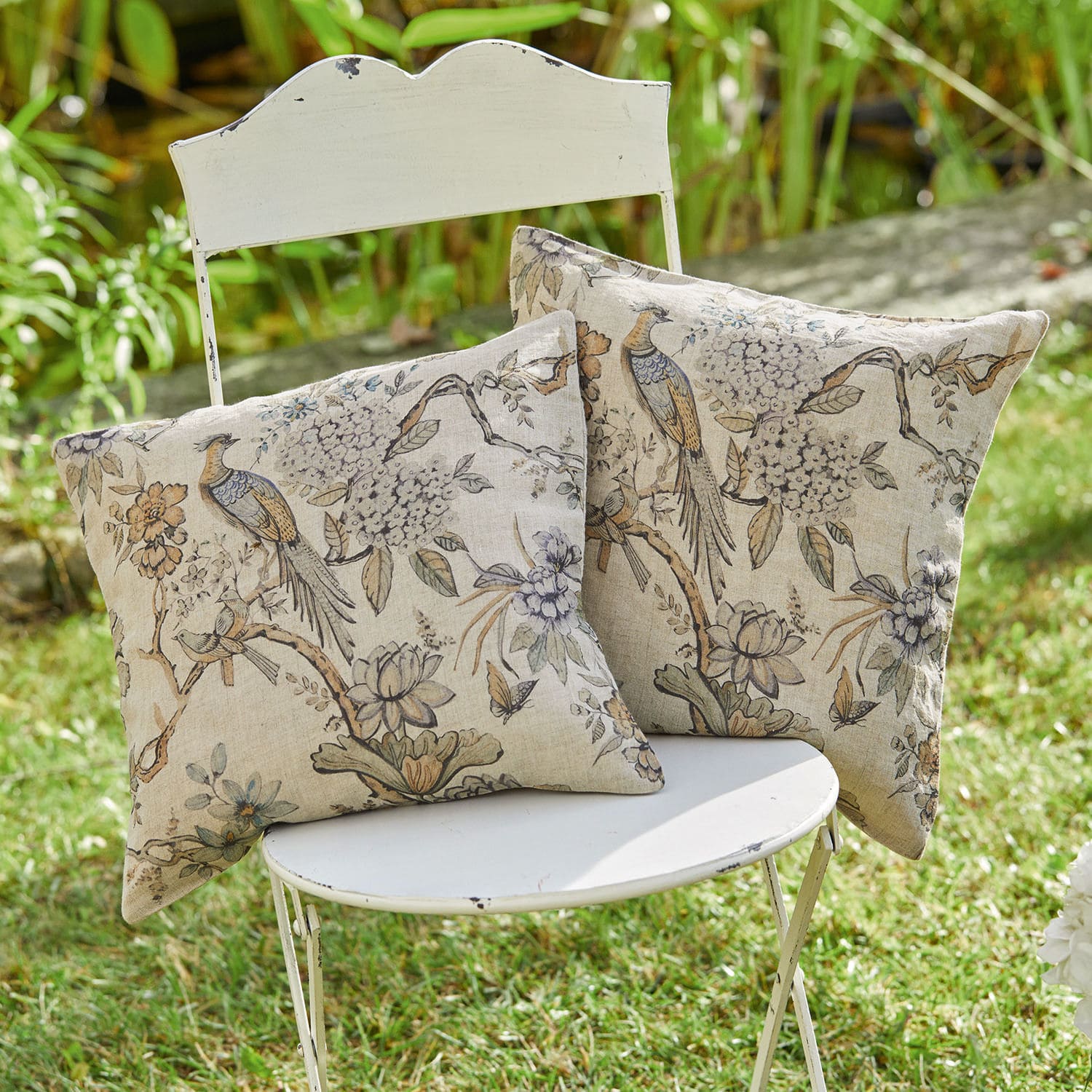 Coppia di copricuscini Lorry Due cuscini decorativi in cotone beige con stampa di uccelli e fiori su sedia bianca in giardino