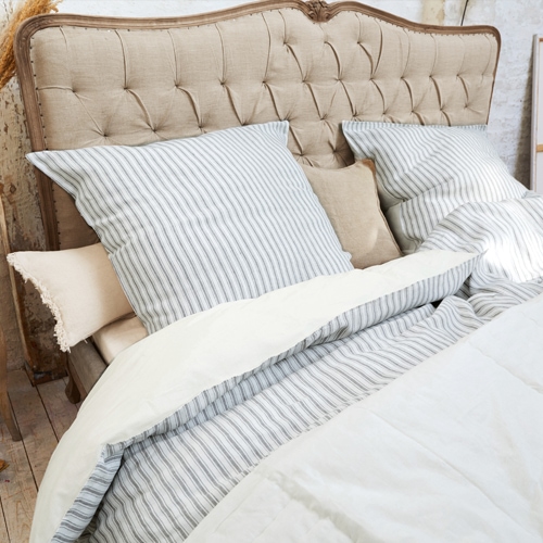 Testiera imbottita beige con biancheria da letto a righe grigie e coperta crema in camera da letto