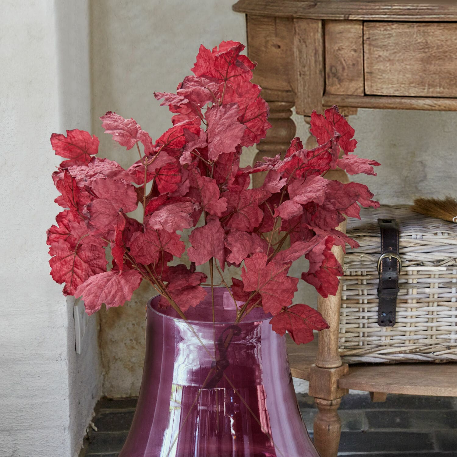 Set di 3 rami decorativi Camirissa Foglie rosse decorative in vaso di vetro viola trasparente davanti a mobile in legno