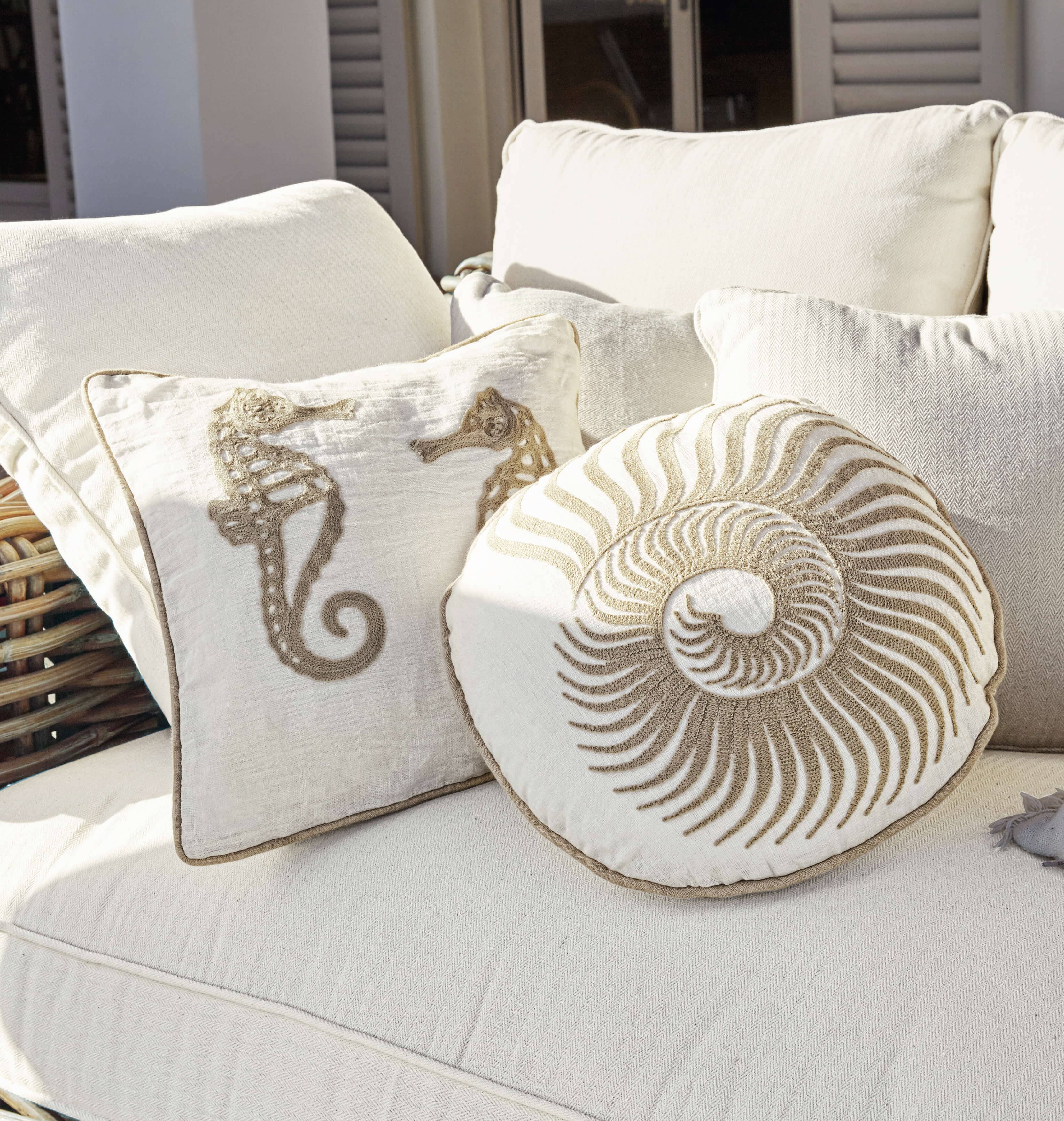 Cuscini decorativi beige con motivi marini su divano chiaro, tessuti per la casa
