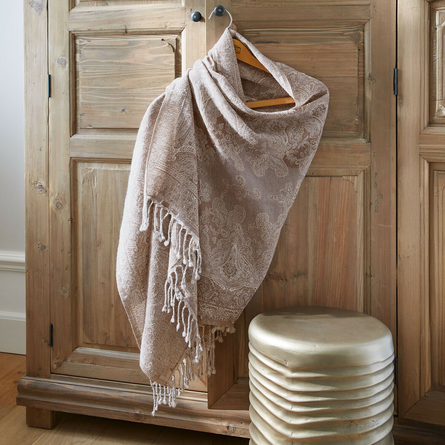 Sciarpa beige con motivo paisley e frange appesa a un armadio in legno, tessuto morbido e decorativo