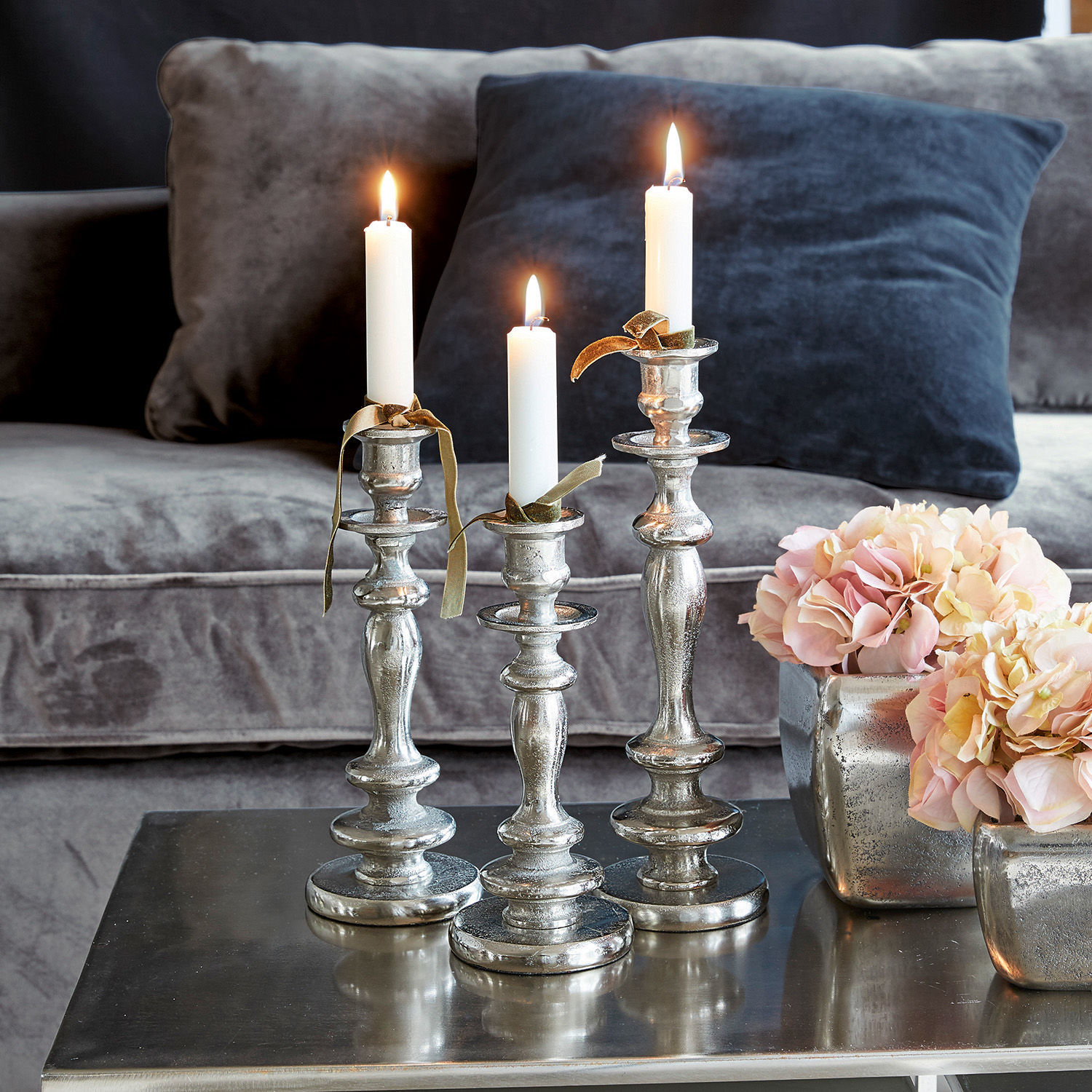 Set di 3 candelieri Borga Set di tre candelabri in metallo argentato con candele bianche su tavolino in soggiorno