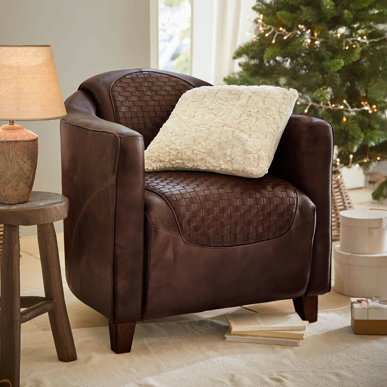 Poltrona Westerdales Poltrona in pelle marrone intrecciata con cuscino crema, ambiente accogliente con lampada e albero di Natale