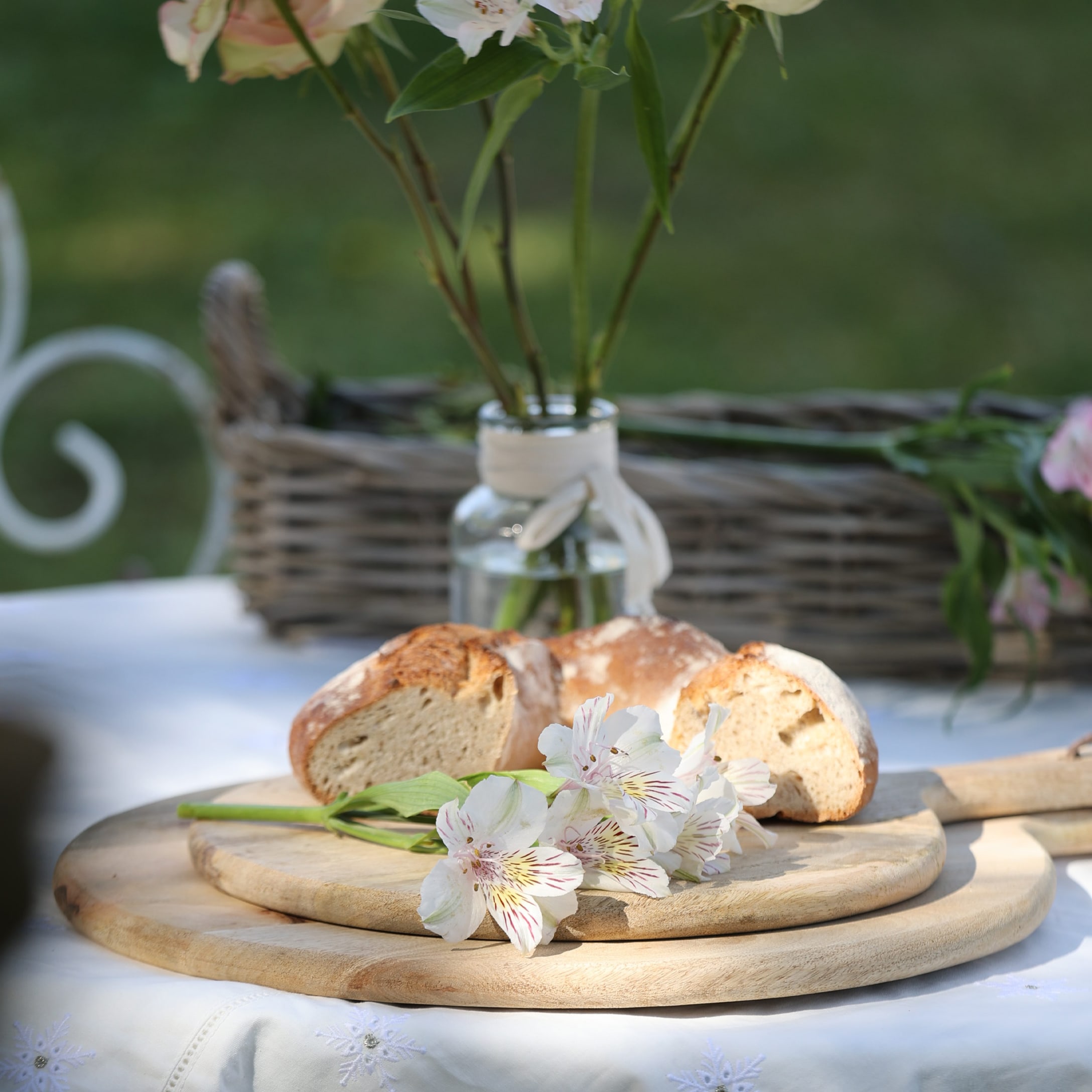 Tagliere in legno con pane e fiori bianchi su tavolo da giardino all'aperto