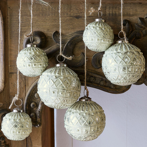 Set di sei palline decorative bianche con motivo, appese a corde su sfondo in legno