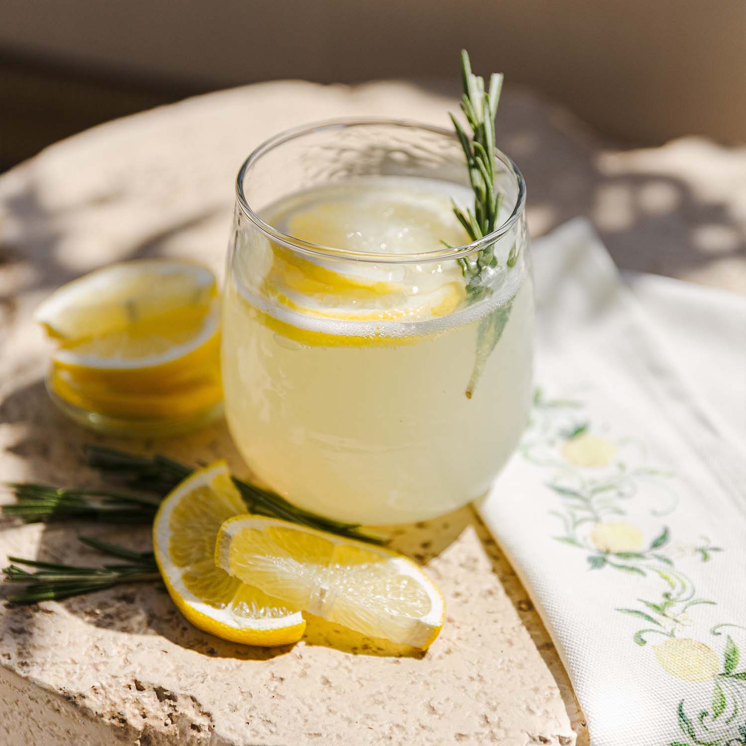 Bicchiere di limonata con fette di limone e rametto di rosmarino su superficie in pietra con tovagliolo