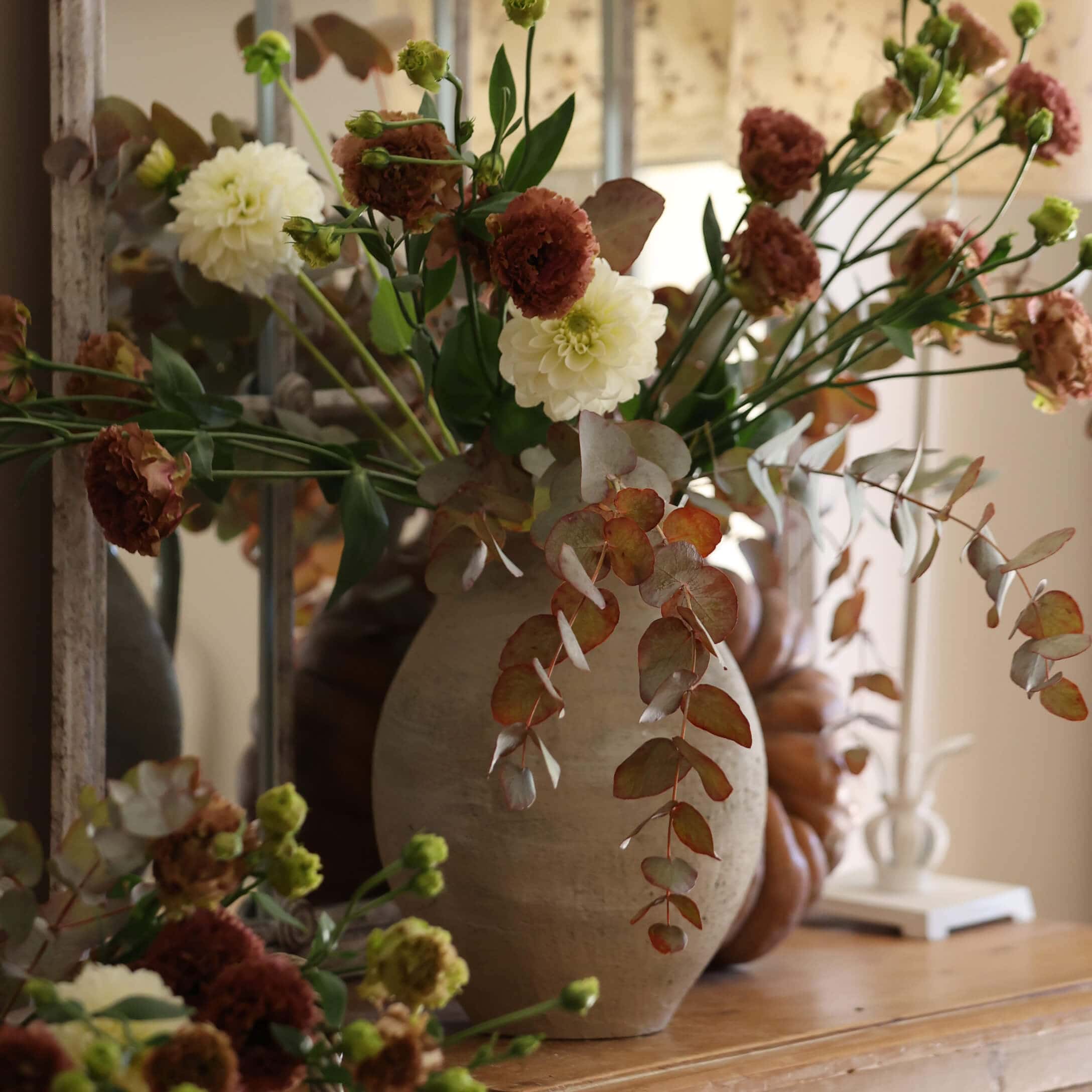 Vaso in ceramica beige con mazzo di fiori bianchi e marroni su tavolo in legno decorativo
