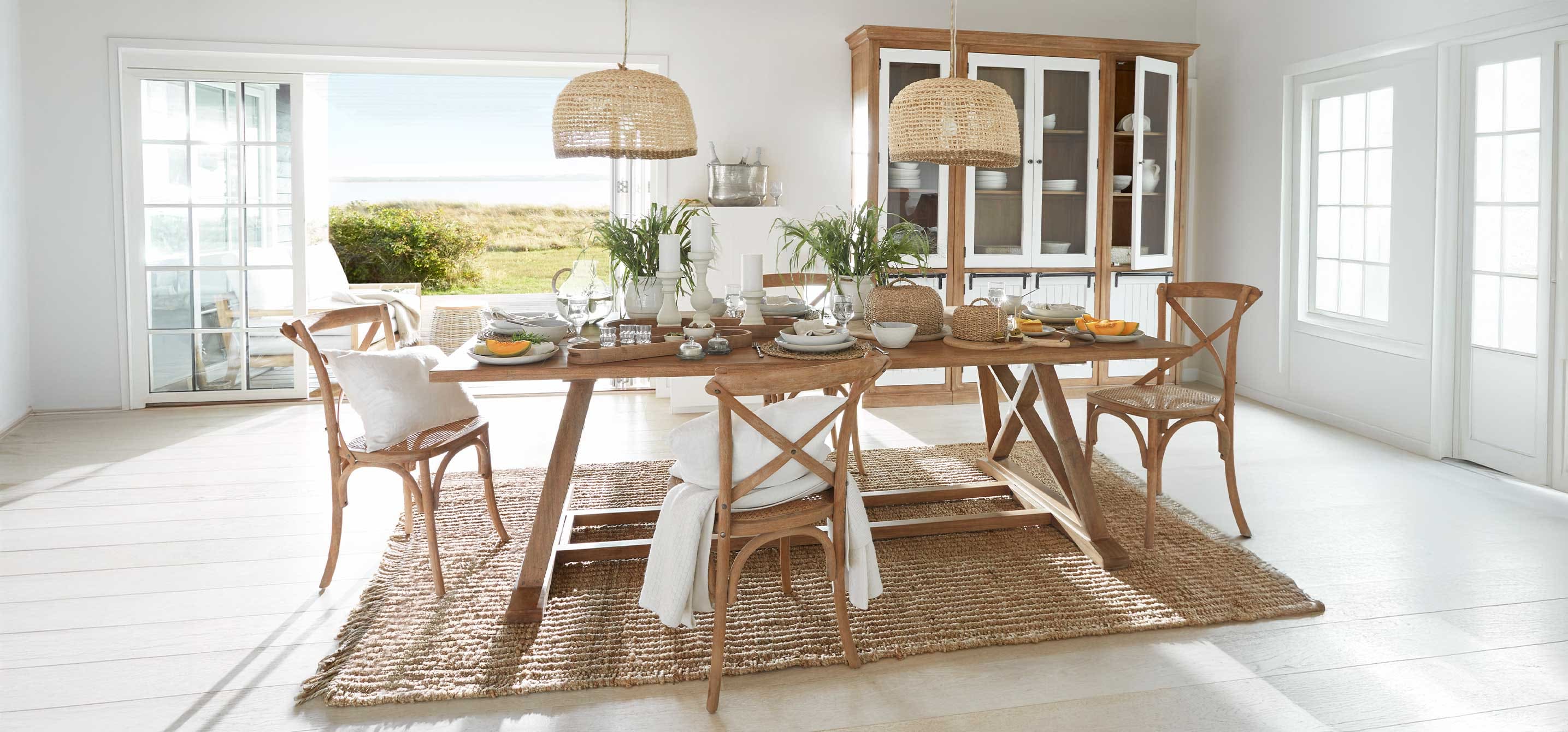 Sala da pranzo con tavolo e sedie in legno naturale, lampade in vimini e decorazioni con piante verdi