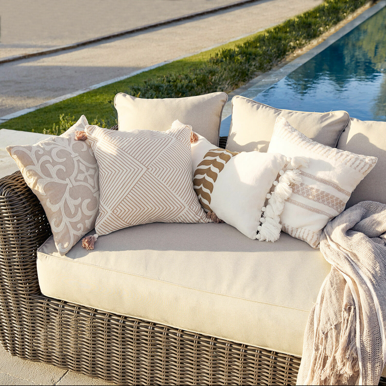 Set di 4 copricuscini Olette Divano in rattan beige con cuscini decorativi crema e beige all'aperto vicino alla piscina