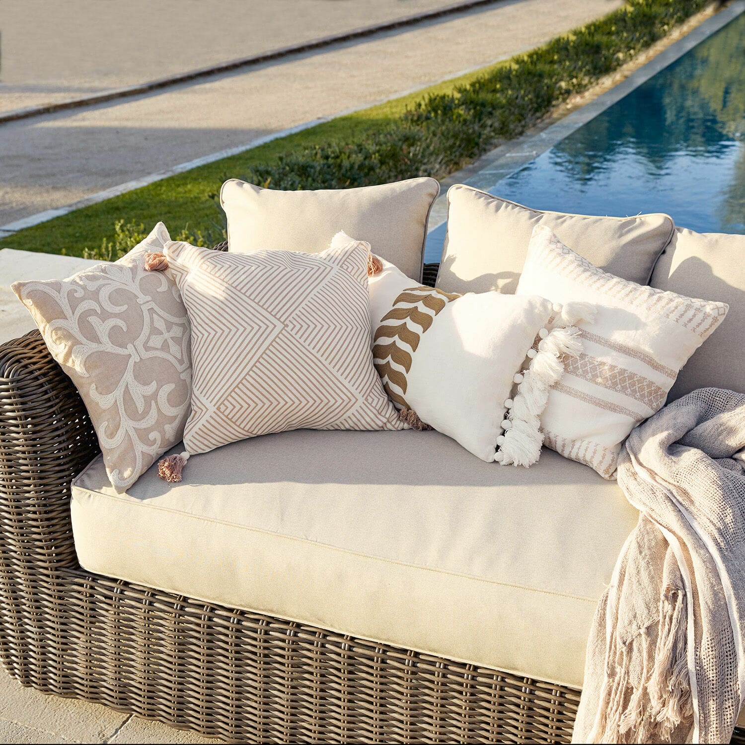 Set di 4 copricuscini Olette Divano in rattan beige con cuscini decorativi crema e beige all'aperto vicino alla piscina