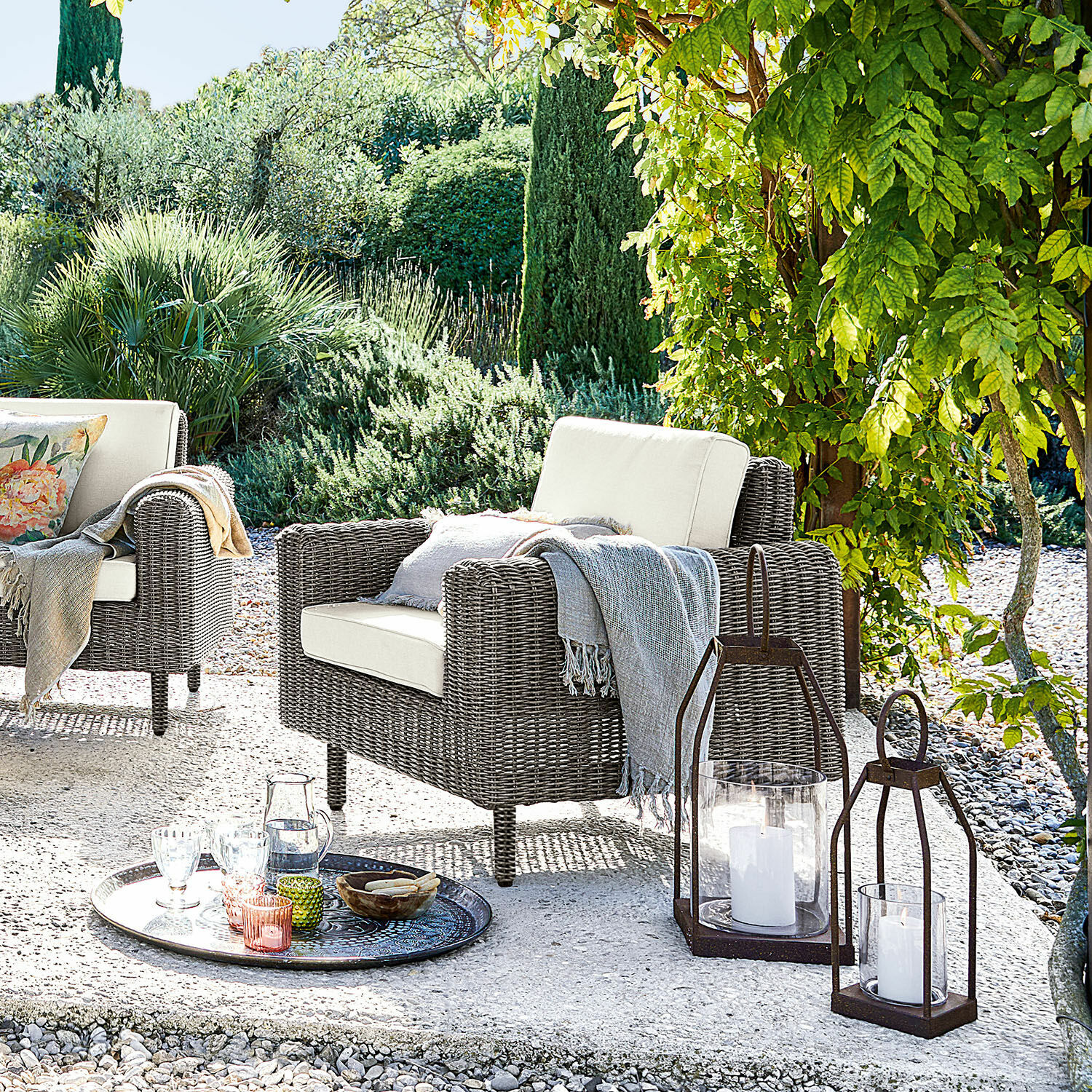 Poltrona Bardou Poltrona da giardino in rattan grigio con cuscini crema e lanterne decorative sul patio
