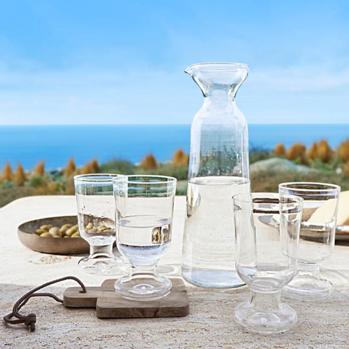 Caraffa di vetro e quattro bicchieri trasparenti su tavolo con vista mare, vetro chiaro