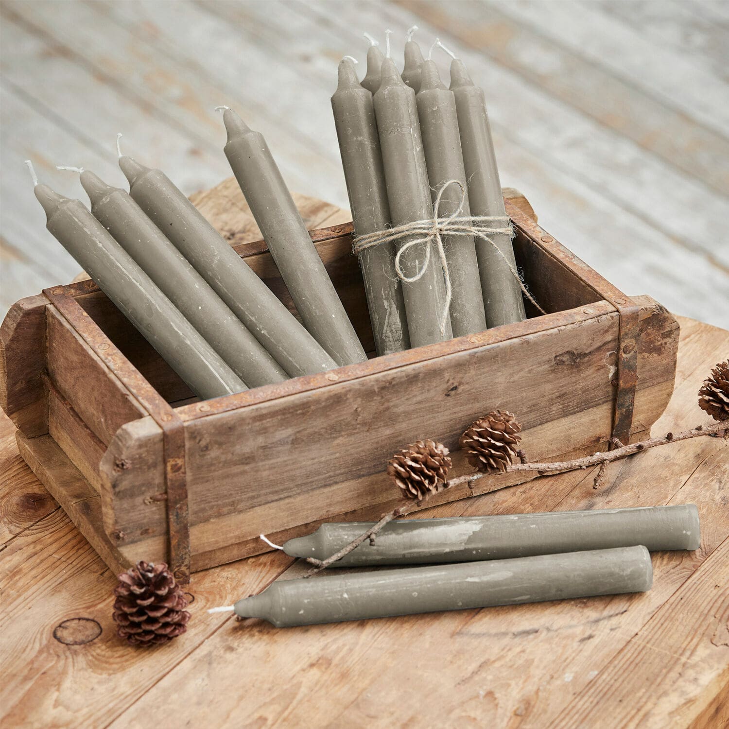 Set di 12 candele Bauceau Candele da tavola grigie in cera in cassetta di legno su tavolo rustico con pigne