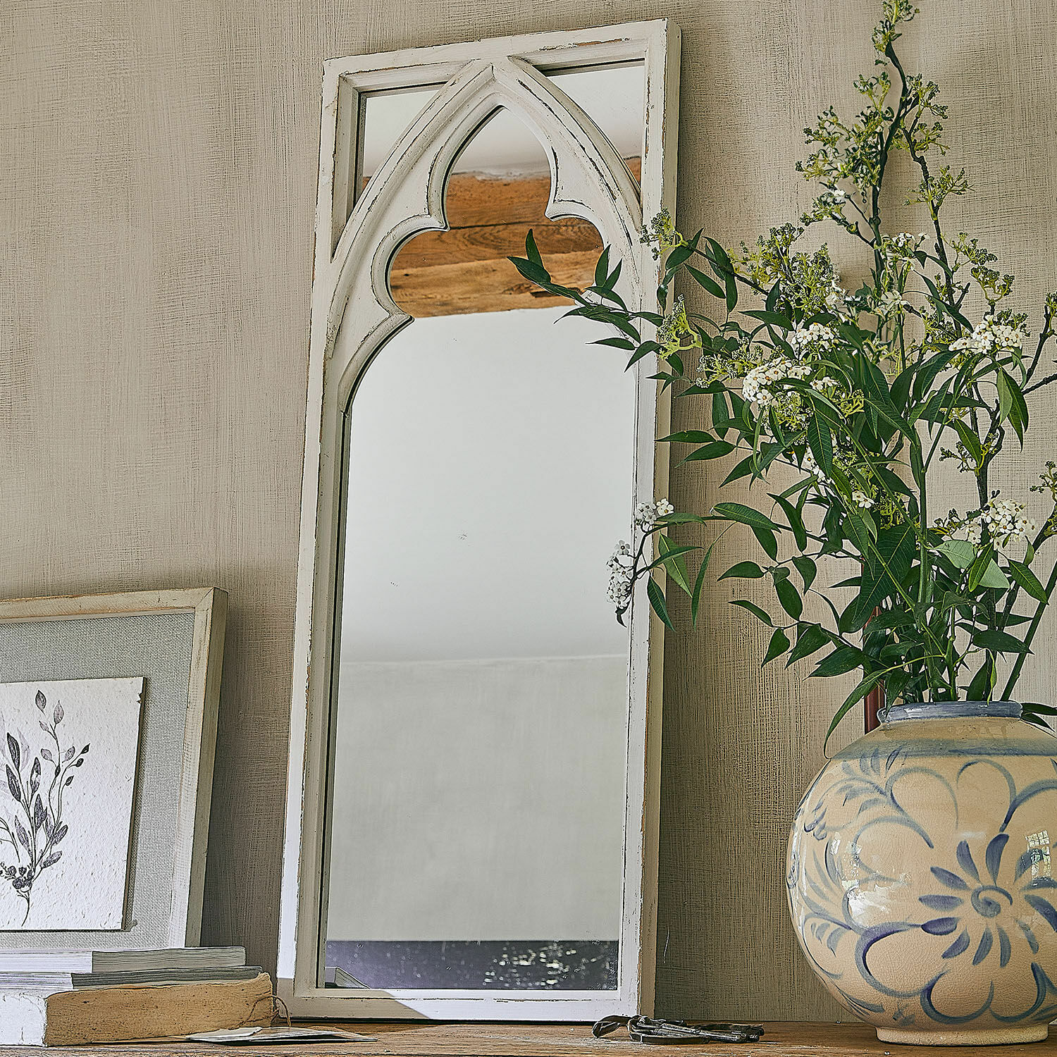 Specchio Golvine Specchio in legno bianco con motivo gotico su tavolo in legno accanto a vaso decorativo con fiori