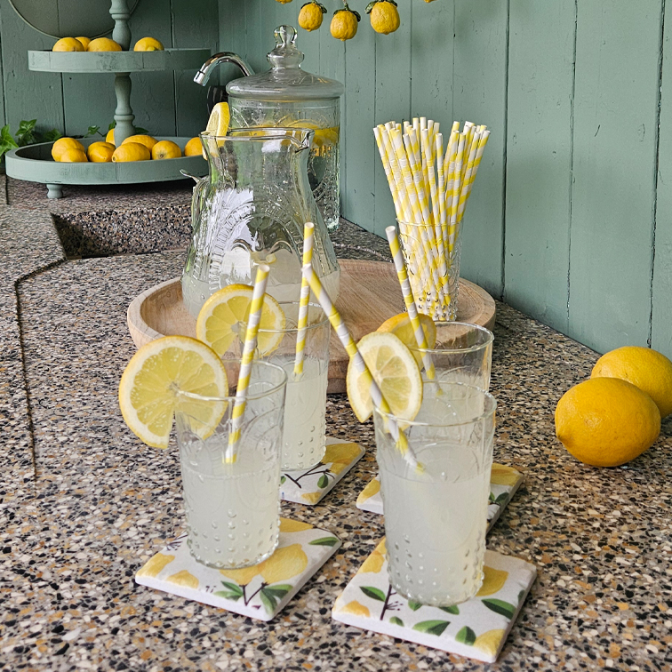 Bicchieri di limonata con fette di limone su piano in pietra con cannucce di carta e vassoio con limoni