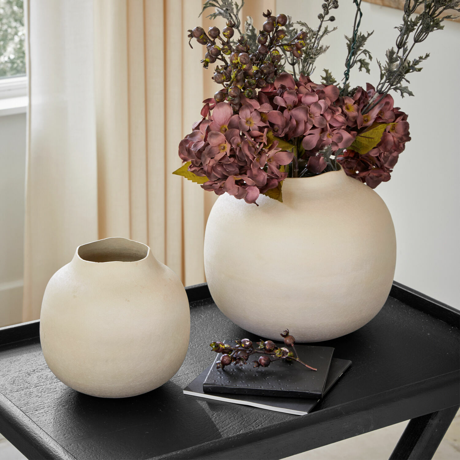 Coppia di vasi Fleurons Due vasi in ceramica color crema su tavolo nero con fiori decorativi e libri sullo sfondo