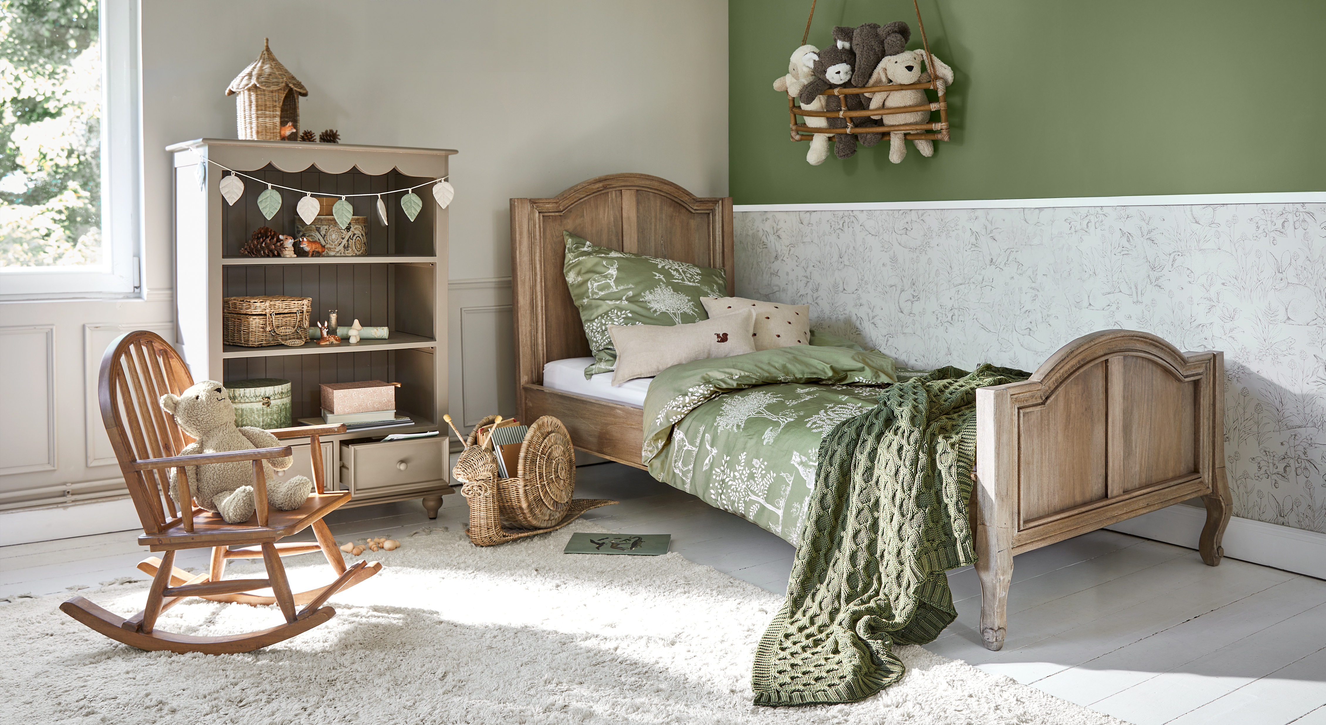 Letto per bambini in legno con biancheria verde e coperta, stanza accogliente con sedia a dondolo e peluche