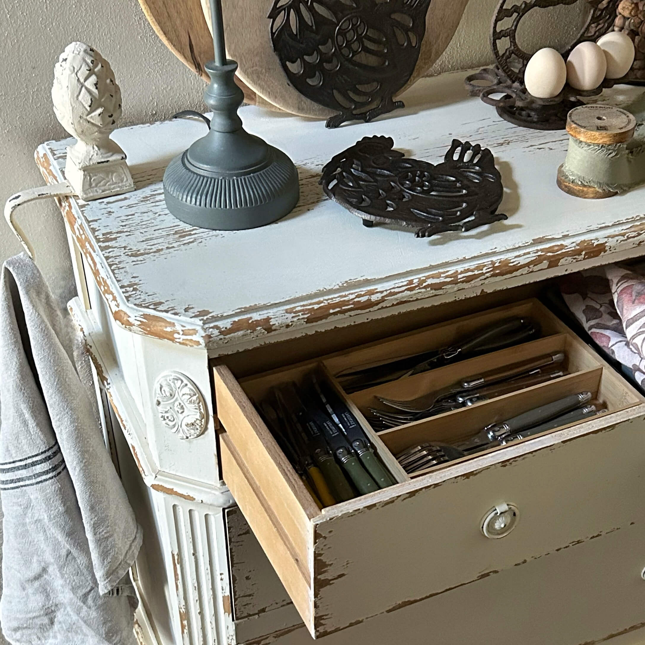 Comò in legno bianco in stile shabby con cassetto aperto e posate organizzate, stile rustico