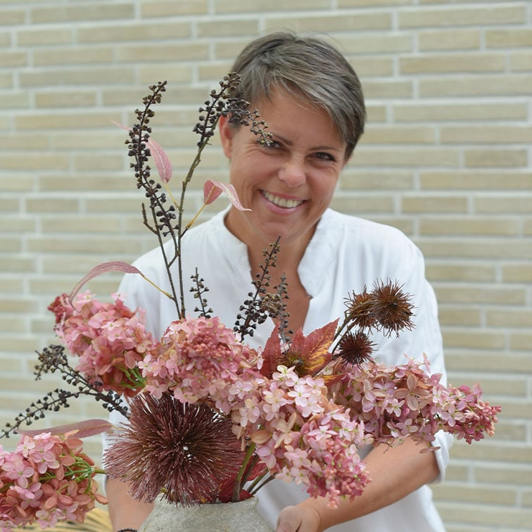 Donna con camicia bianca che tiene un vaso con fiori secchi decorativi rosa e marroni