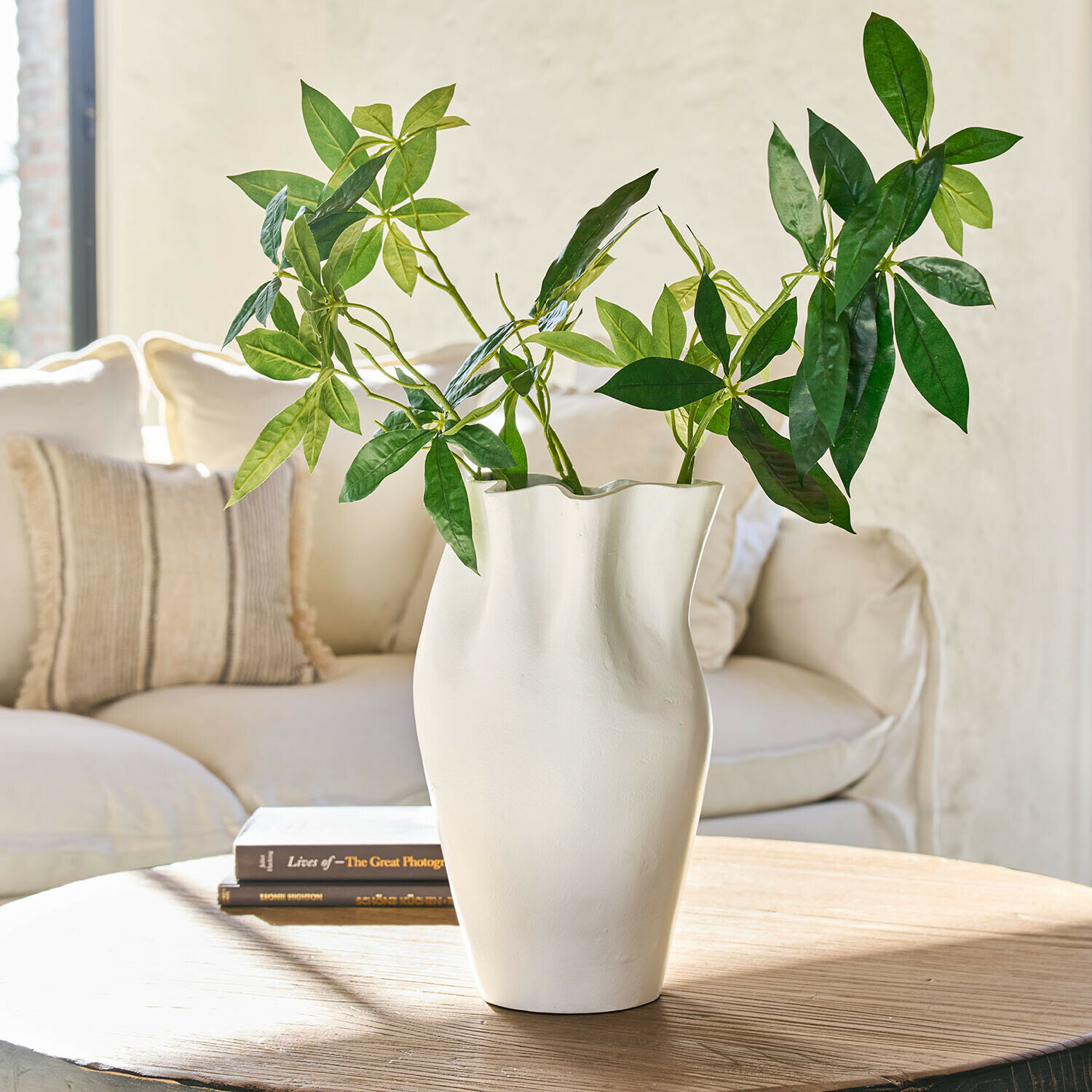Vaso Palomira Vaso bianco in ceramica dalla forma ondulata con foglie verdi su tavolo in legno in soggiorno