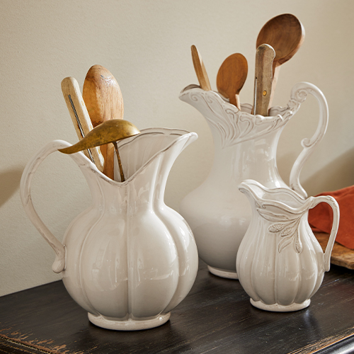 Set di tre brocche in ceramica bianca con motivo decorativo, contenenti cucchiai di legno da cucina