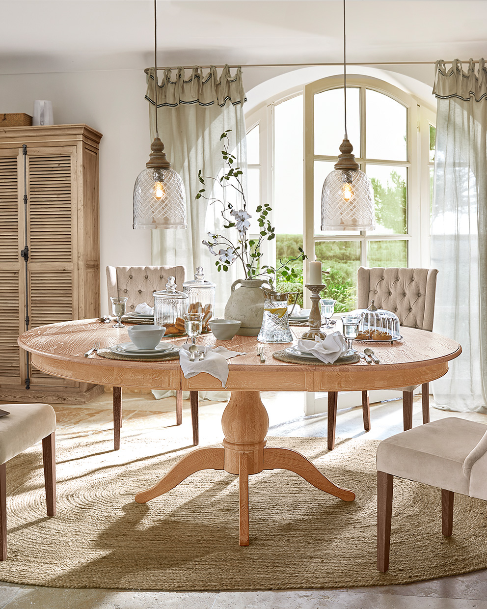 Tavolo da pranzo ovale in legno chiaro con sedie beige e decorazioni da tavola in stile rustico