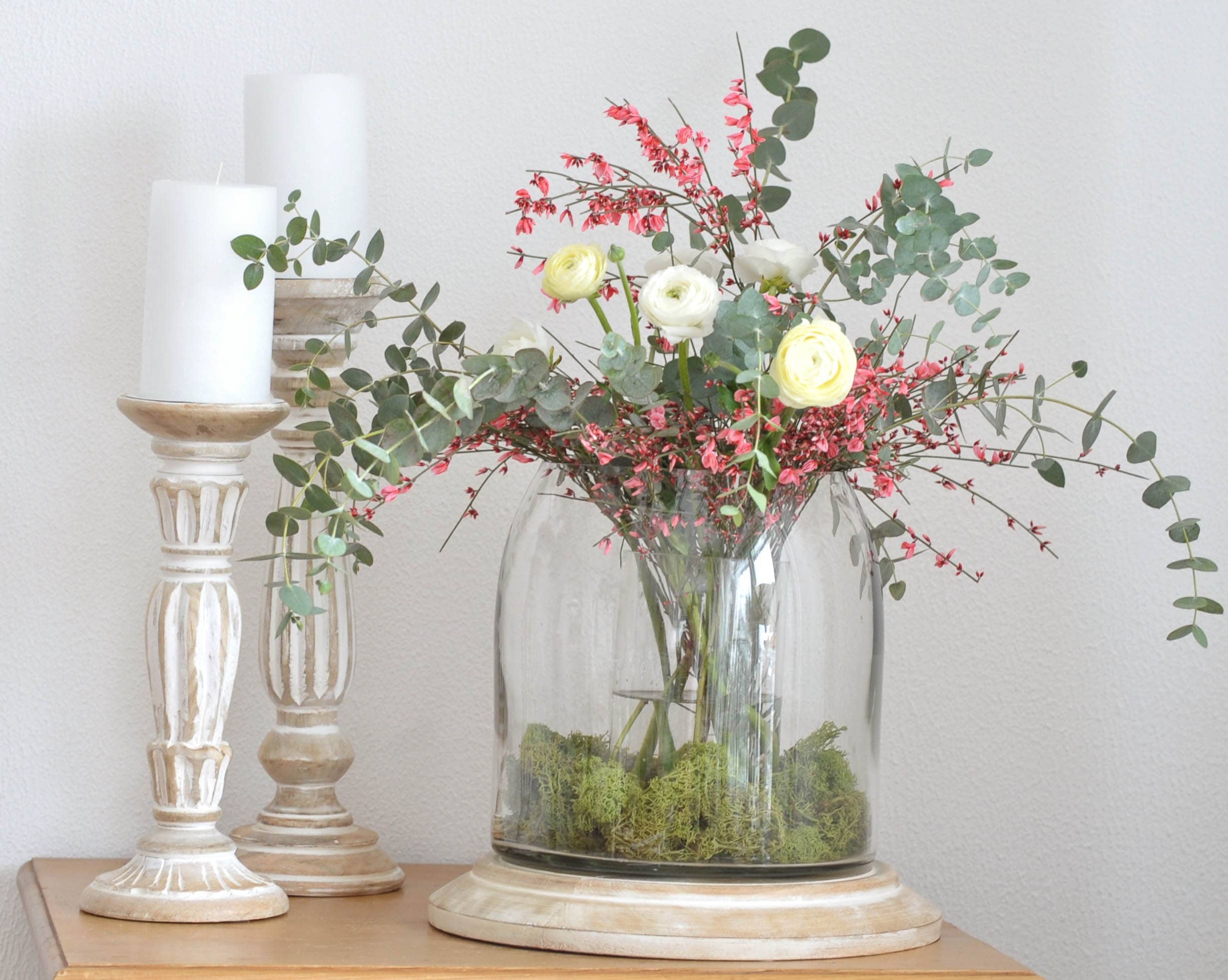 Bouquet decorativo di fiori bianchi e rosa in vaso di vetro su base in legno con candele bianche