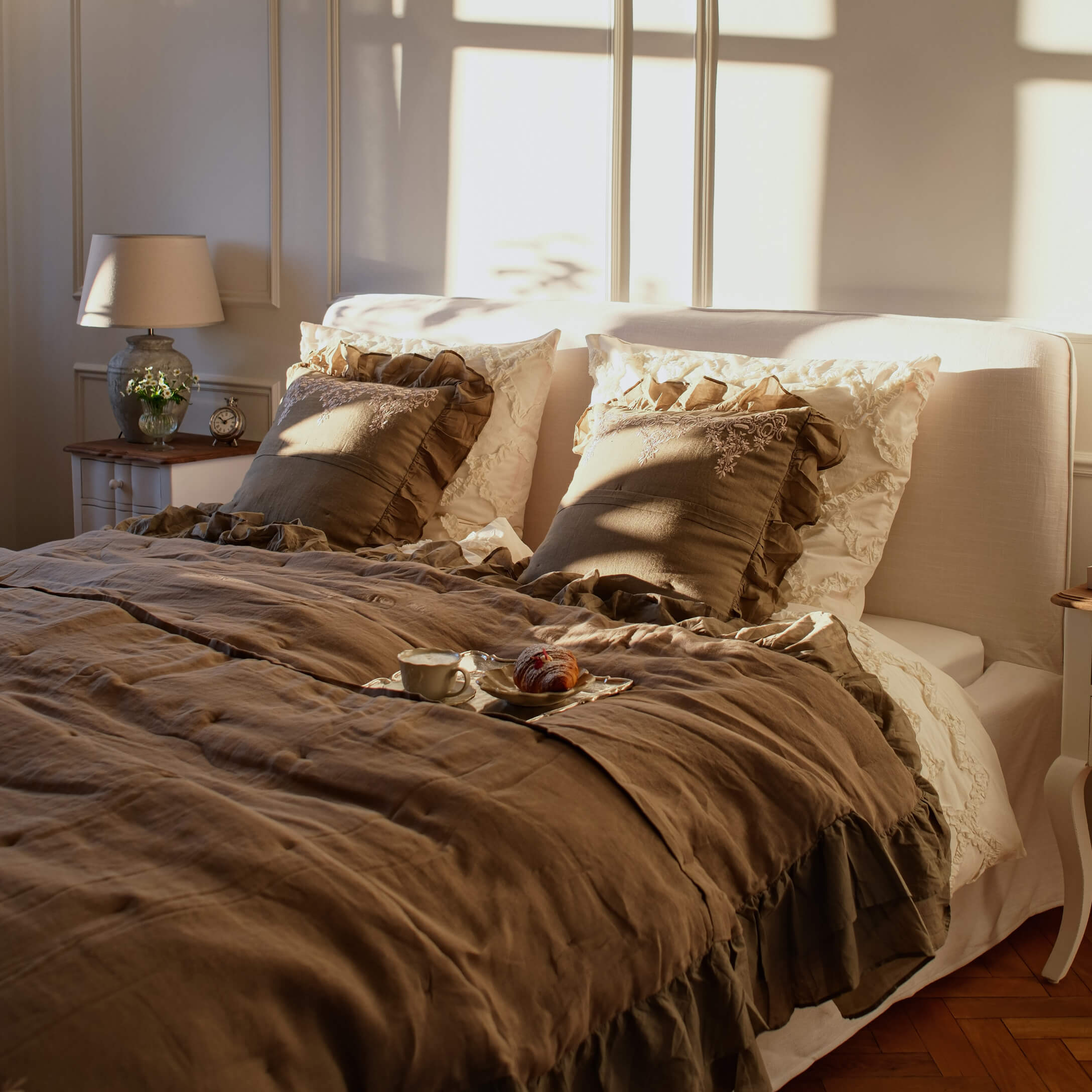 Camera accogliente con biancheria da letto in lino beige e cuscini marroni con volant alla luce calda