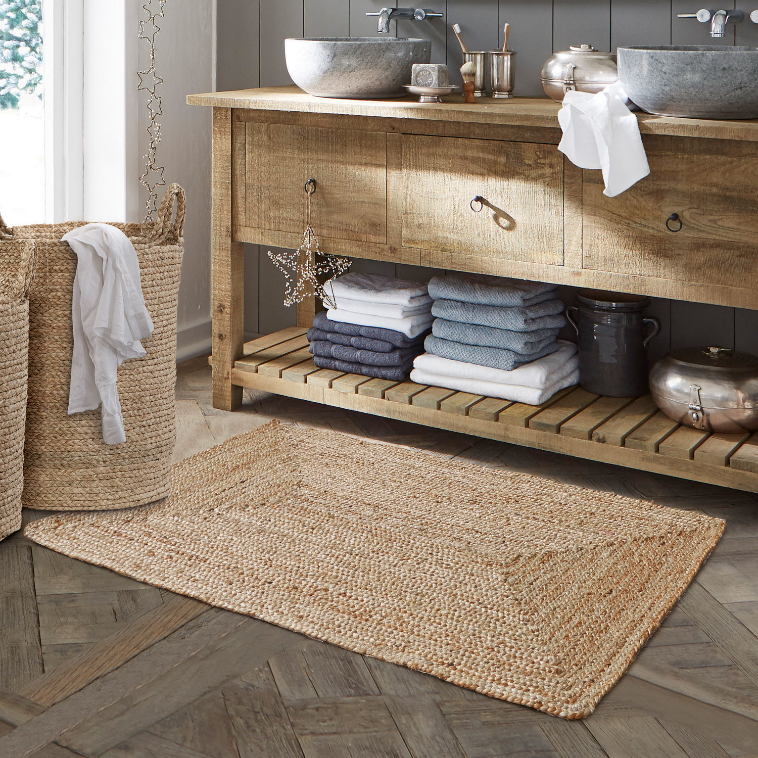 Scendibagno Busselton Tappeto da bagno beige in juta naturale su pavimento in legno con cesta per biancheria intrecciata