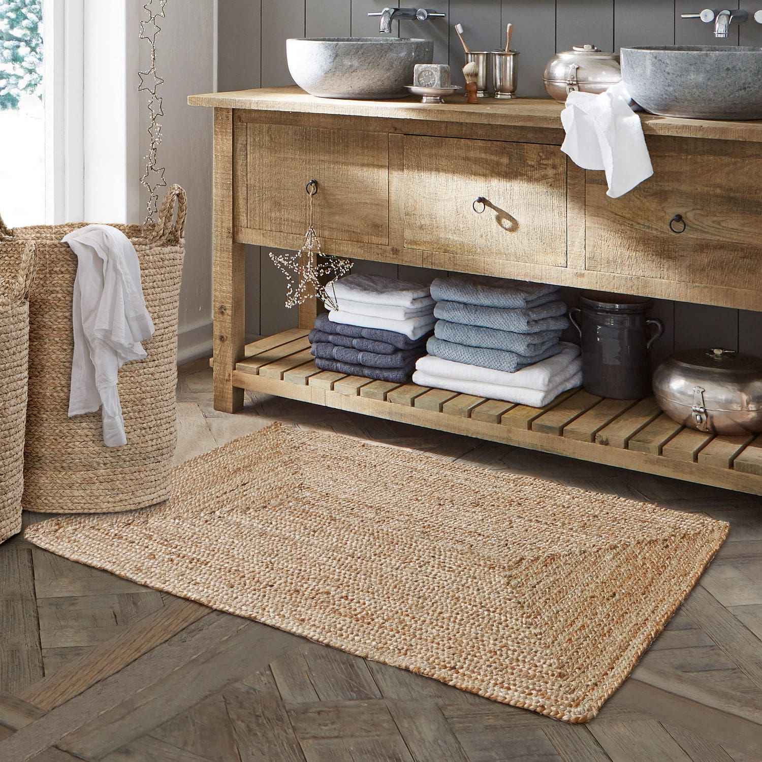 Scendibagno Busselton Tappeto da bagno beige in juta naturale su pavimento in legno con cesta per biancheria intrecciata