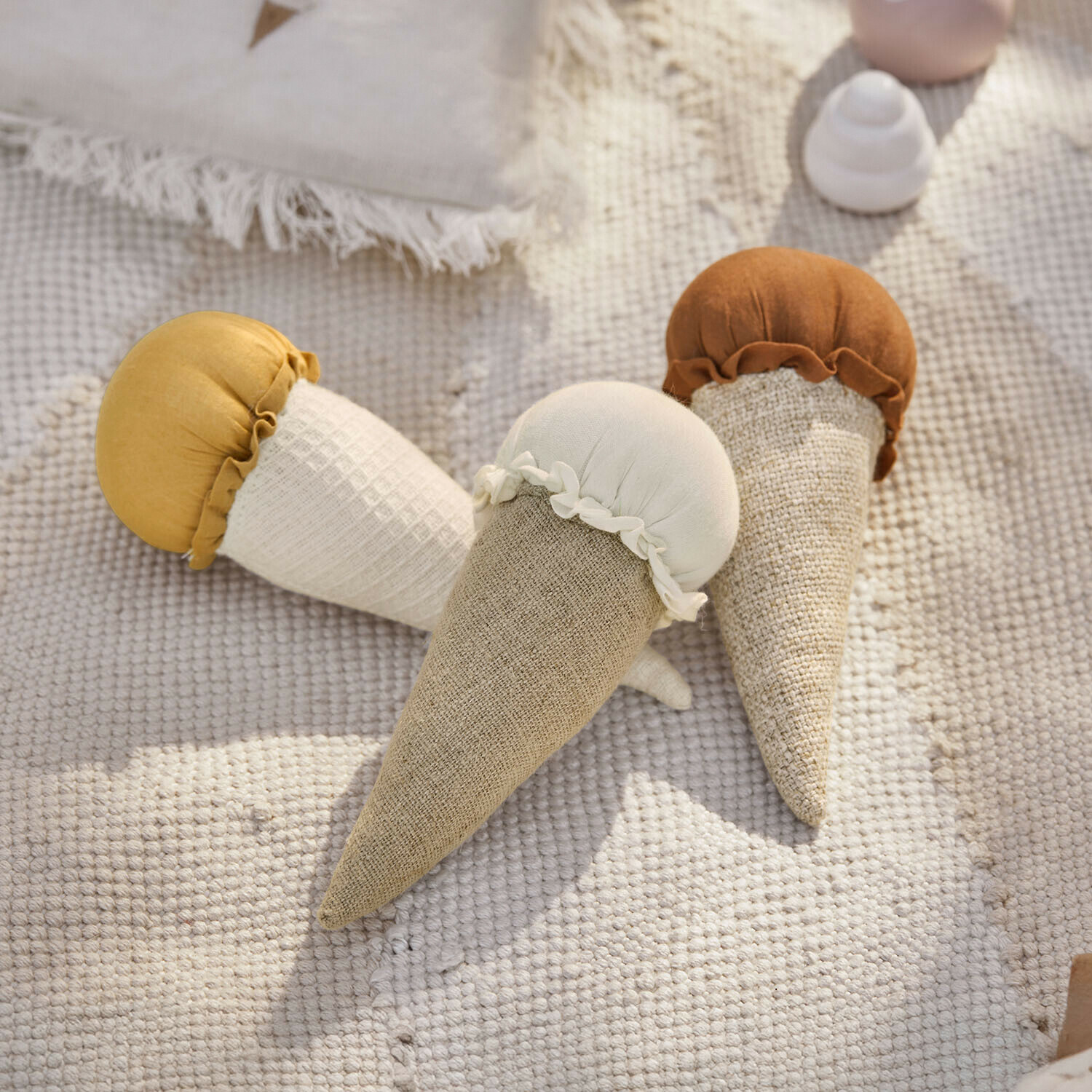 Set di 3 giocattoli Cheeklee Tre giocattoli morbidi in tessuto a forma di cono gelato in beige, bianco e marrone su tappeto chiaro