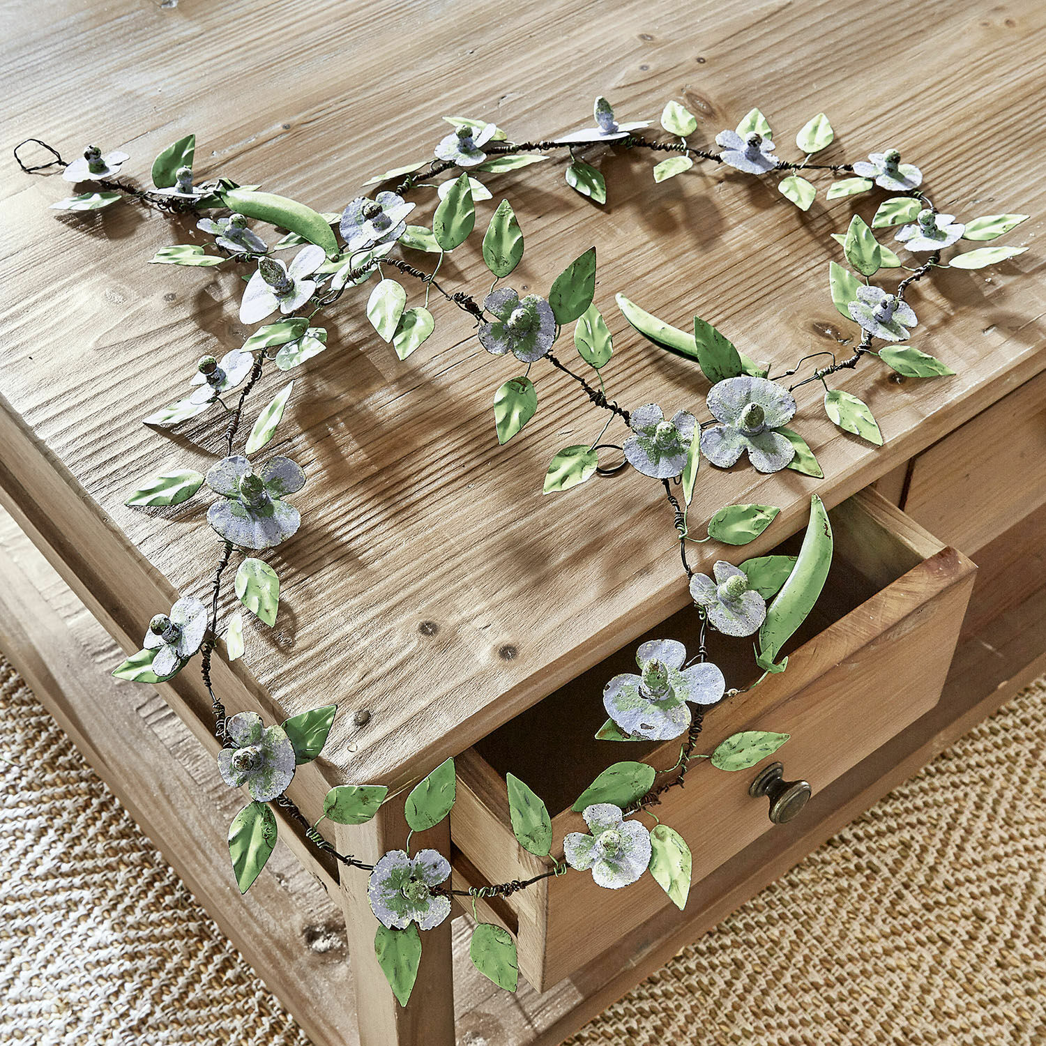 Festone Cecilia Corona decorativa in metallo con fiori e foglie verdi e grigie su tavolo in legno chiaro