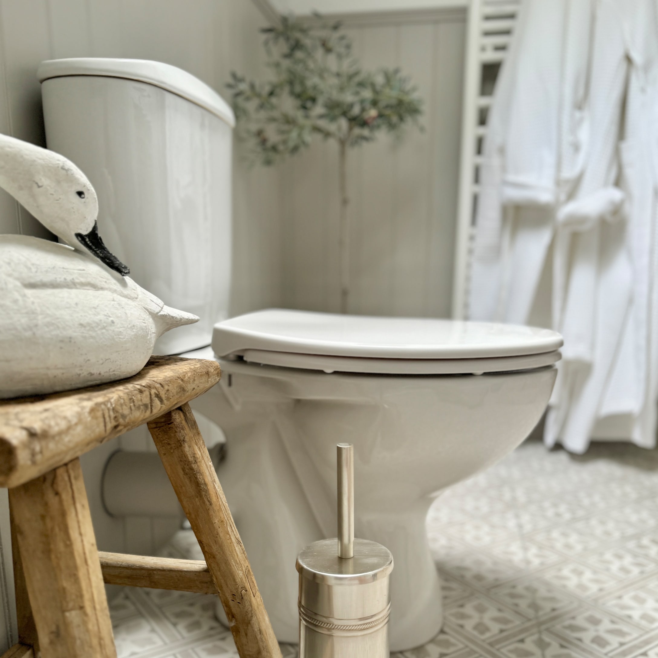 WC in ceramica bianca con spazzola metallica e sgabello in legno in bagno con decorazione a cigno