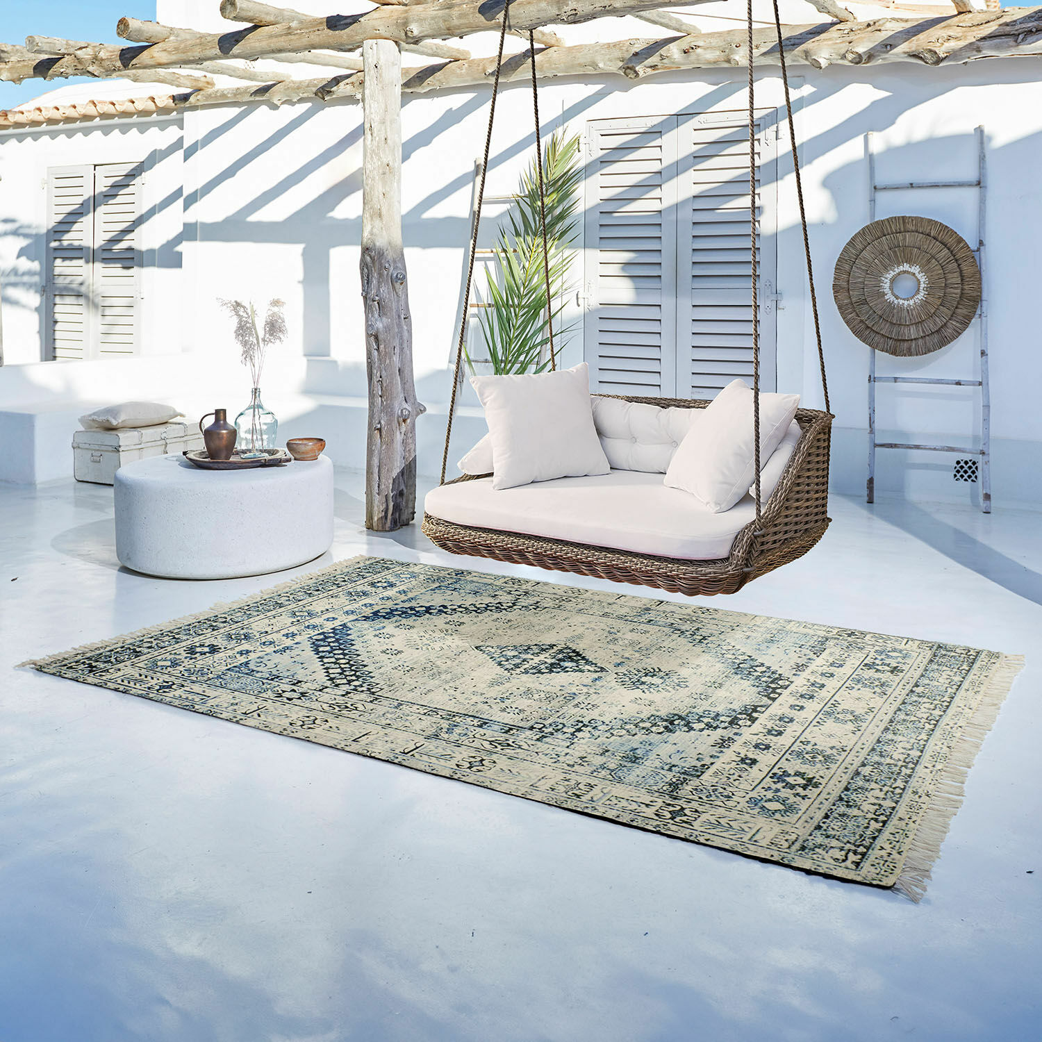 Tappeto per esterni e interni Daly Tappeto vintage beige e azzurro su pavimento chiaro accanto a dondolo in rattan con cuscini bianchi