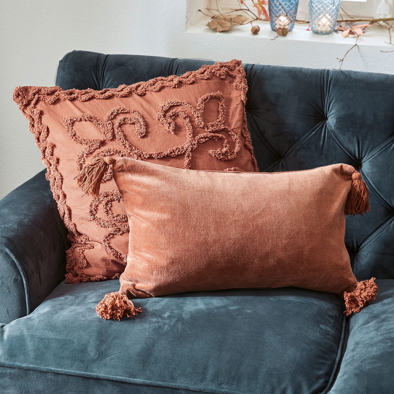 Coppia di copricuscini Posadas Due cuscini decorativi in velluto arancione su divano blu scuro, accessori morbidi e di stile per il soggiorno