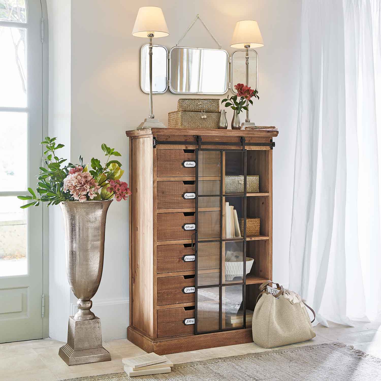 Comò in legno con cassetti e porta in vetro in interno luminoso con decorazioni e lampade