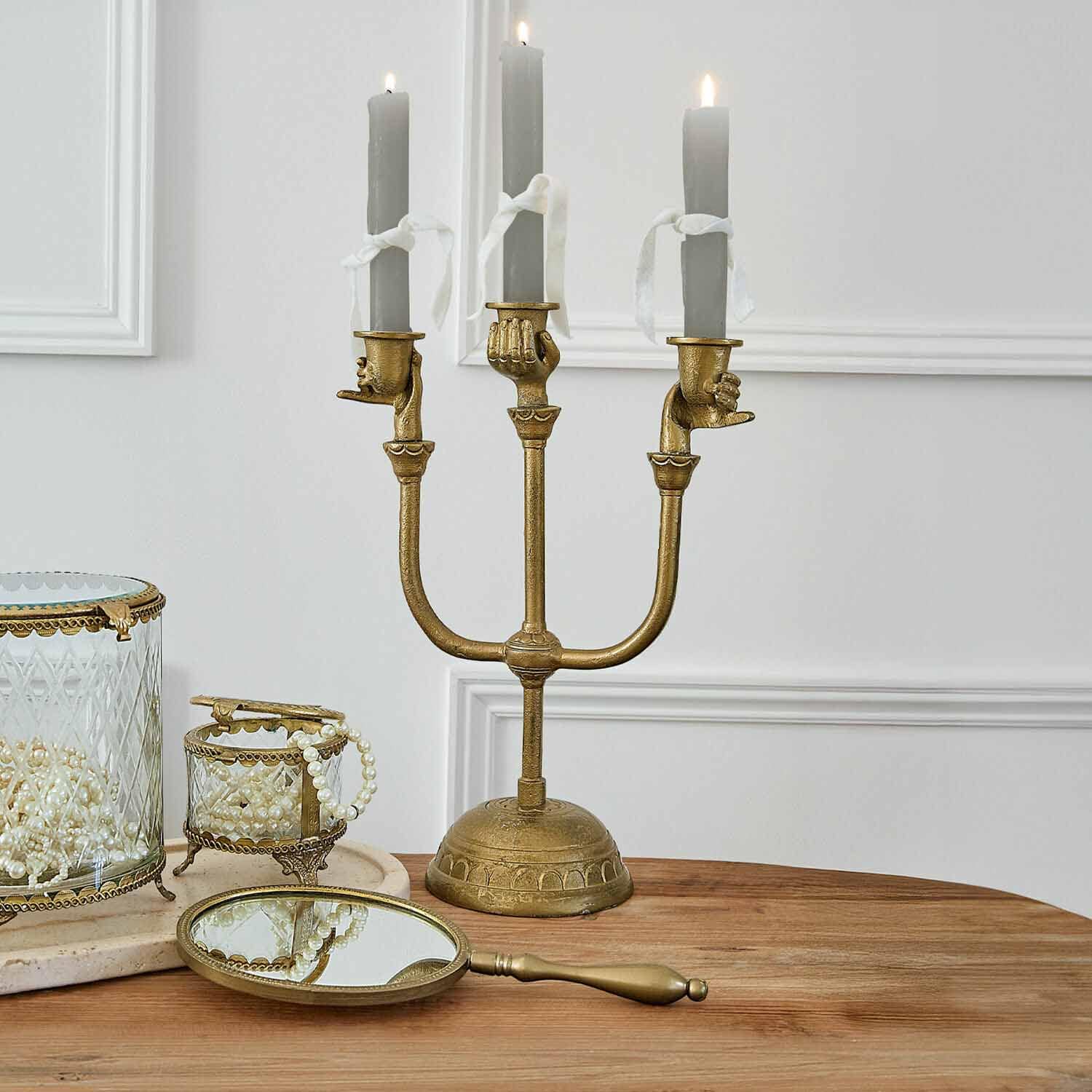 Candelabro dorato con tre candele grigie tenute da mani, decorazione da tavolo con specchio e scatole per gioielli